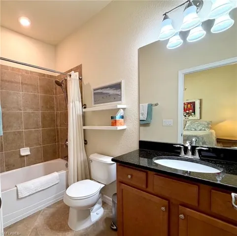 Ensuite bathroom with shower / bath combo with shower curtain, vanity, light tile patterned floors, and a chandelier