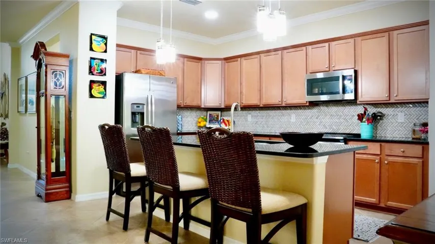 Kitchen featuring decorative backsplash, an island with sink, stainless steel appliances, ornamental molding, and a breakfast bar