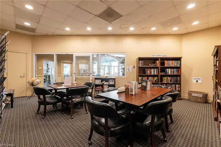Carpeted library space featuring multiple dark wood tables, upholstered armchairs, and built-in bookshelves