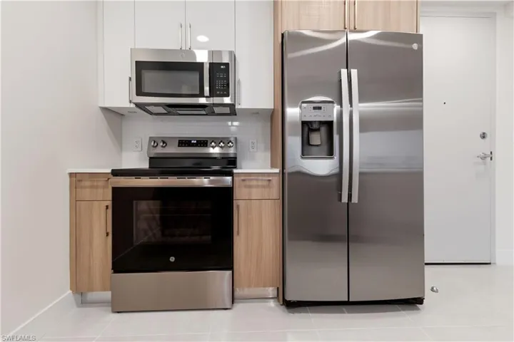 Contemporary kitchen featuring full-size stainless steel appliances, light wood-finish lower cabinetry, white upper cabinetry, and a white subway tile backsplash