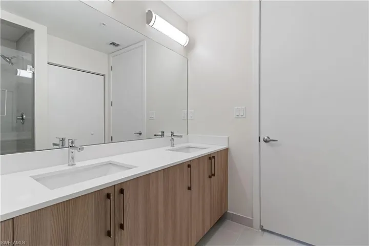 Double vanity featuring integrated rectangular sinks, chrome faucets, and a light wood-finish cabinetry