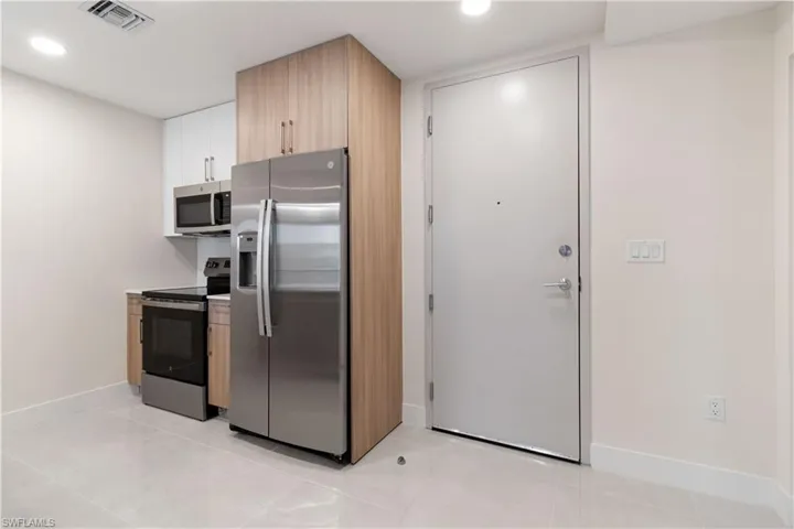 Modern kitchen area featuring stainless steel appliances, light wood-finish cabinetry, white upper cabinets, white countertops, and light-toned tile flooring