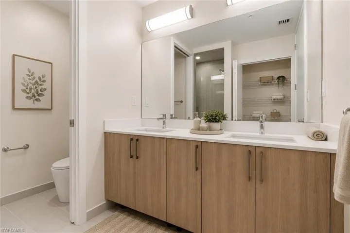Double vanity with light wood-finish cabinetry, chrome fixtures, and a spacious countertop