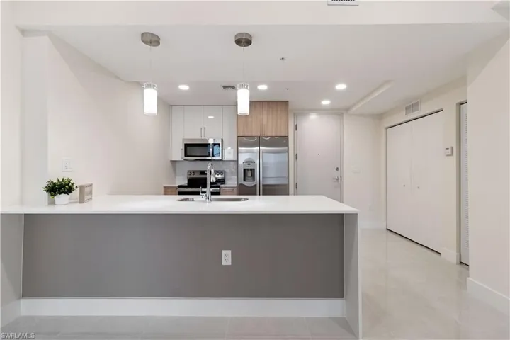Modern kitchen featuring a light-toned countertop island with pendant lighting, stainless steel appliances, and two-tone cabinetry