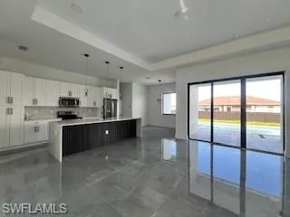 Kitchen featuring a raised ceiling, an island with sink, white cabinets, open floor plan, and hanging light fixtures
