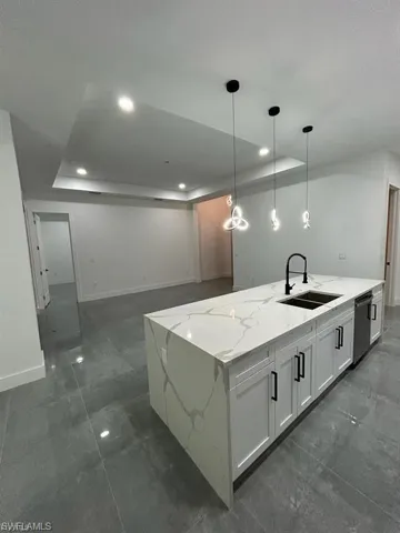 Kitchen featuring a tray ceiling, a spacious island, light stone counters, hanging light fixtures, and white cabinetry
