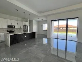 Kitchen featuring white cabinetry, hanging light fixtures, a center island, stainless steel microwave, and fridge