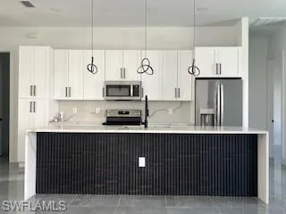 Kitchen featuring white cabinetry, pendant lighting, appliances with stainless steel finishes, and a spacious island
