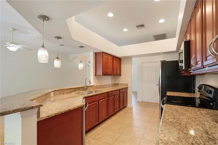 Kitchen featuring a peninsula, pendant lighting, a tray ceiling, light stone countertops, and stainless steel appliances