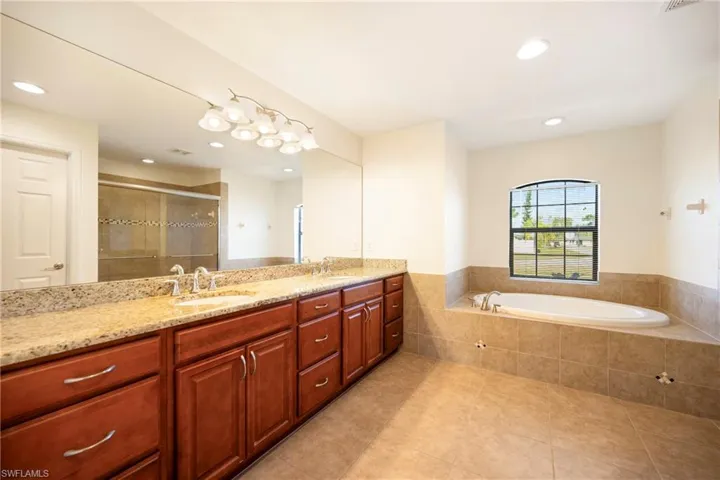 Full bath featuring double vanity, a stall shower, a garden tub, recessed lighting, and light tile patterned floors