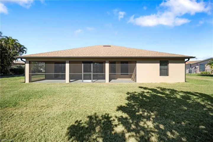 Back of property with a shingled roof, a lawn, a sunroom, and stucco siding