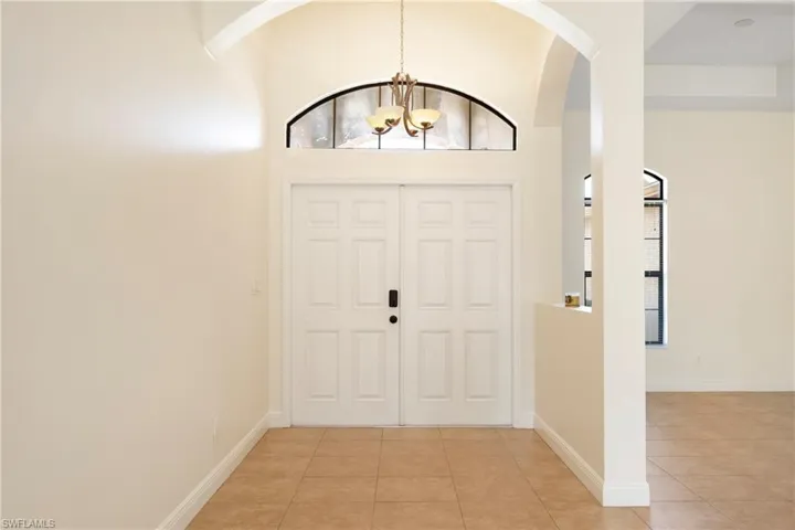 Foyer entrance featuring suspended lighting, light tile patterned flooring, a high ceiling, and arched walkways