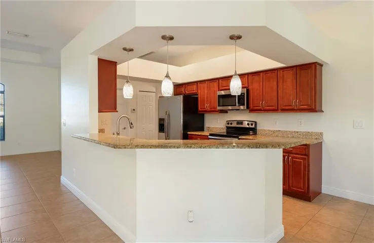 Kitchen with a raised ceiling, hanging light fixtures, stainless steel appliances, light stone counters, and light tile patterned floors