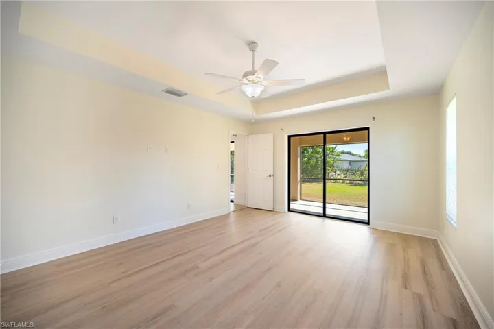 Spare room featuring light wood finished floors, a tray ceiling, and ceiling fan