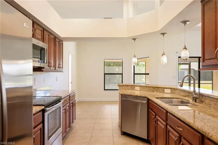 Kitchen featuring stainless steel appliances, pendant lighting, light stone counters, and light tile patterned floors