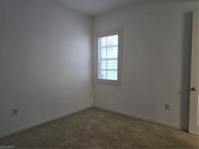 Neutral wall finishes, carpet flooring, a window with plantation shutters, and a white door