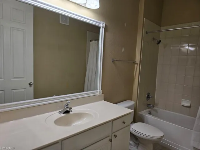 Vanity with integrated sink, white cabinetry, chrome faucet, wall-mounted mirror, and a bathtub with tiled surround