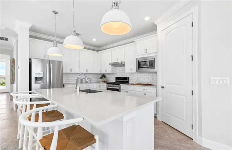 Kitchen featuring tasteful backsplash, pendant lighting, an island with sink, sink, and appliances with stainless steel finishes