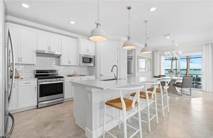 Kitchen featuring appliances with stainless steel finishes, backsplash, a kitchen island with sink, light tile patterned flooring, and a chandelier