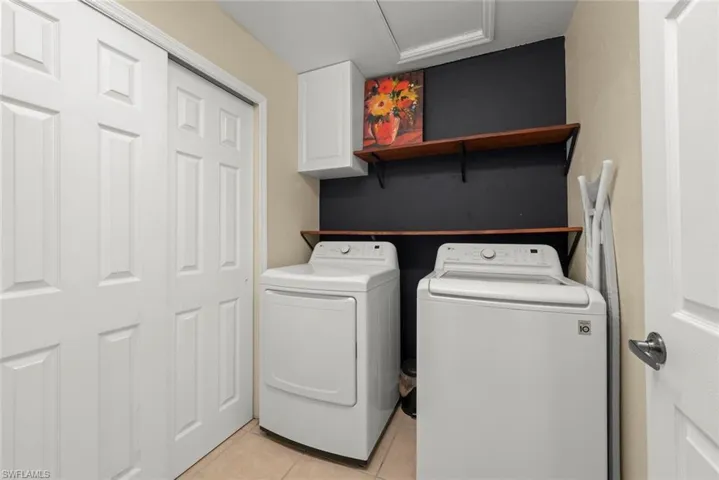 Laundry room featuring tile floors, washing machine and dryer, shelving, and a cabinet