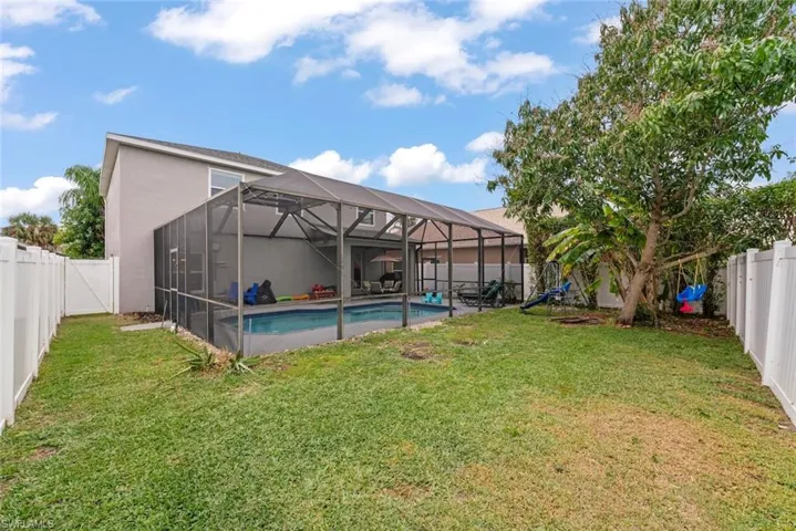 Rear view of home featuring a lanai, pool, fruit trees, and fenced yard