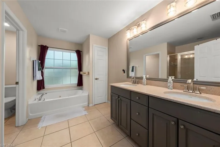 Primary bathroom with double vanity, a toilet closet, light tile patterned floors, and a bathtub