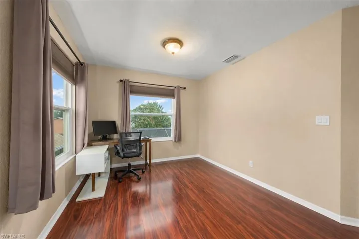 Spacious primary bedroom featuring rich wood-finish flooring, light tan wall finishes, and multiple windows