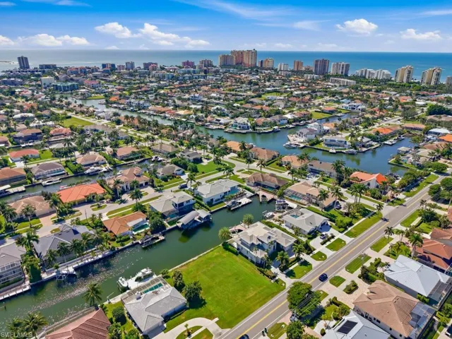 Aerial perspective of a coastal residential community featuring waterfront canal access, boat slips, mature palm trees, and proximity to the oceanfront skyline