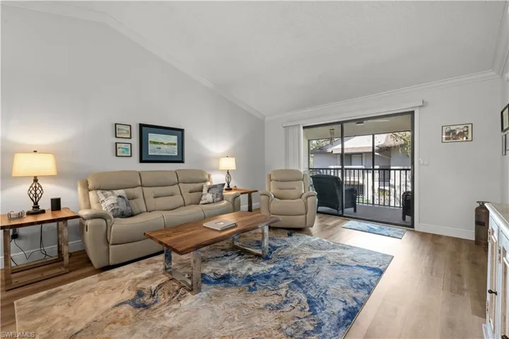 Living room with baseboards, vaulted ceiling, wood finished floors, and ornamental molding