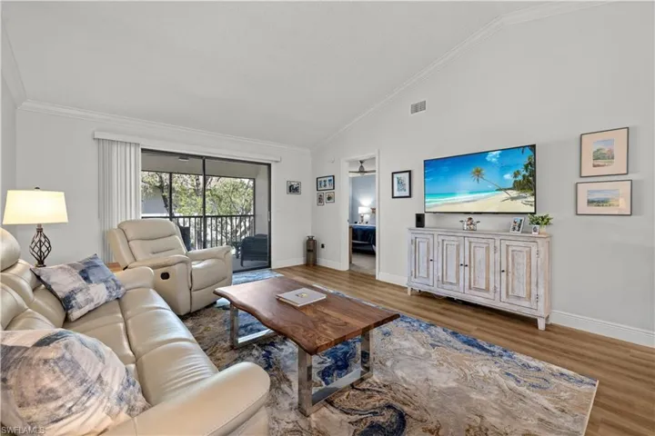 Living room featuring wood finished floors, ornamental molding, baseboards, and high vaulted ceiling