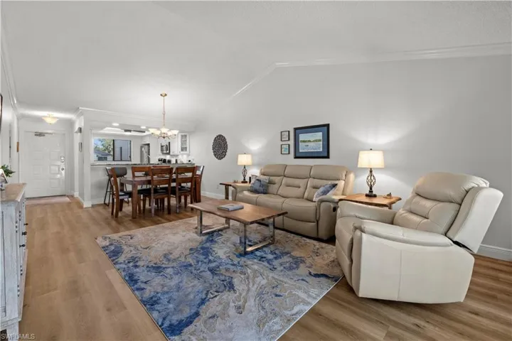 Living room featuring vaulted ceiling, ornamental molding, a chandelier, wood finished floors, and baseboards