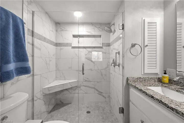 Bathroom featuring toilet, vanity, and a marble finish shower