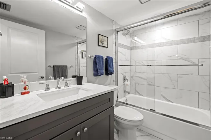 Full bath featuring marble finish flooring, vanity, toilet, and enclosed tub / shower combo
