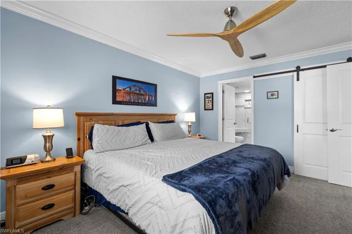 Carpeted bedroom featuring crown molding, a barn door, ensuite bathroom, ceiling fan, and a textured ceiling