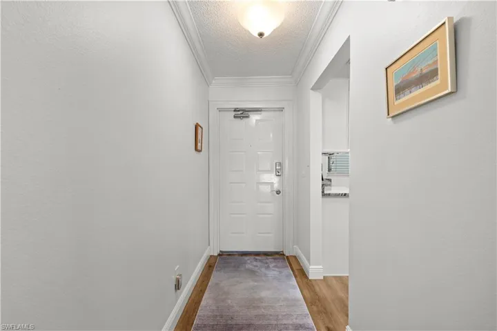 Doorway with a textured ceiling, wood finished floors, ornamental molding, and baseboards