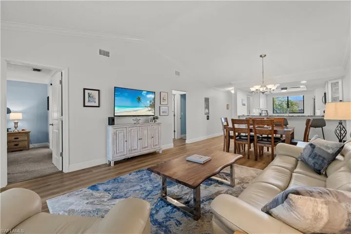 Living room featuring wood finished floors, a chandelier, ornamental molding, lofted ceiling, and baseboards