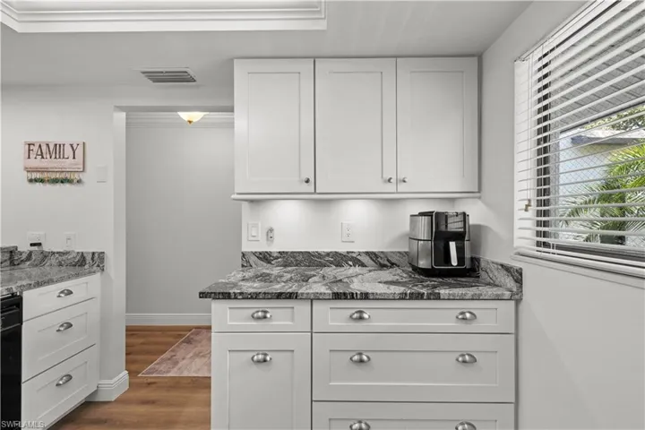 Kitchen with dark stone counters, white cabinets, dark wood finished floors, baseboards, and dishwasher