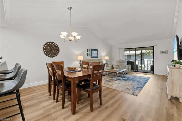 Dining area featuring a chandelier, light wood-style flooring, baseboards, vaulted ceiling, and ornamental molding