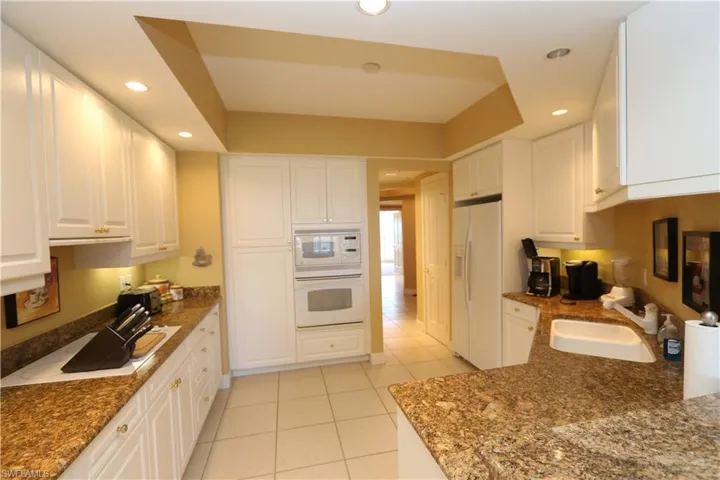 Kitchen featuring white cabinetry, recessed lighting, light tile patterned floors, dark stone countertops, and white appliances