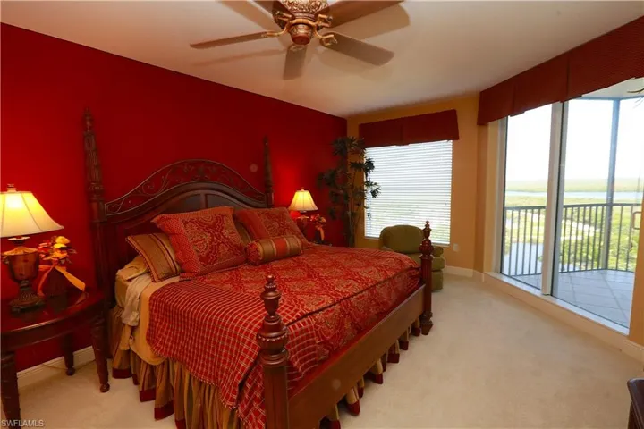 Bedroom featuring light colored carpet, access to exterior, ceiling fan, and a water view