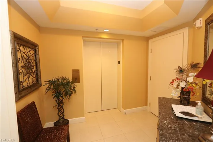 Hall featuring a raised ceiling, light tile patterned flooring, and elevator