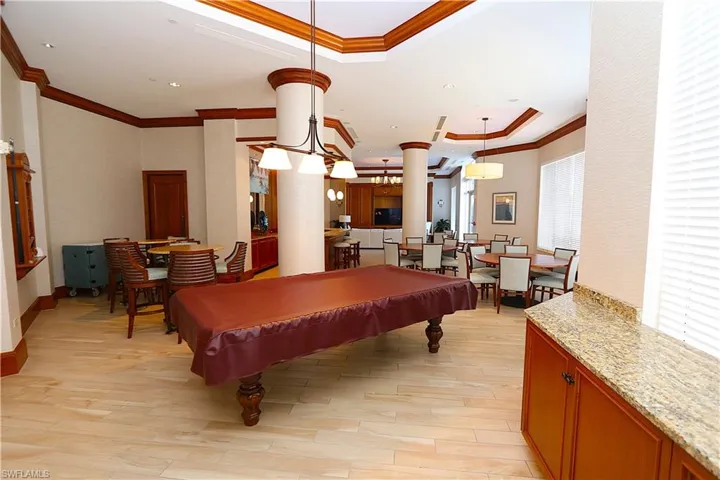 Rec room featuring a tray ceiling, crown molding, billiards table, and light wood-style flooring