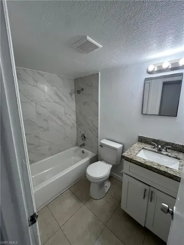 Bathroom with tub / shower combination, vanity, a textured ceiling, a textured wall, and light tile patterned floors