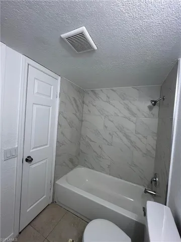 Bathroom featuring shower / bath combination, light tile patterned floors, and a textured ceiling