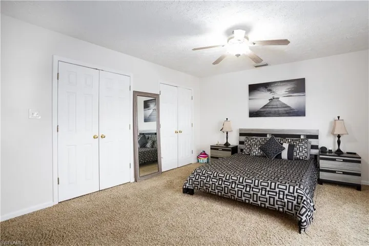 Carpeted bedroom featuring two closets, a textured ceiling, and ceiling fan