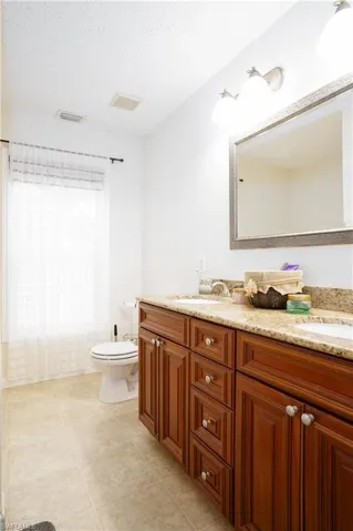 Bathroom with tile patterned floors, a textured ceiling, dual bowl vanity, and toilet