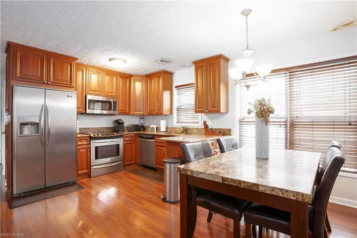 Kitchen with light hardwood / wood-style flooring, a chandelier, a textured ceiling, stainless steel appliances, and decorative light fixtures