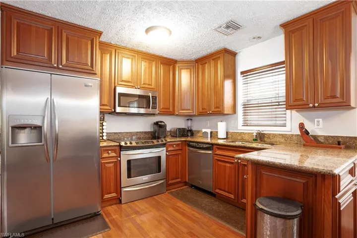 Kitchen featuring stone counters, appliances with stainless steel finishes, wood-type flooring, and a textured ceiling