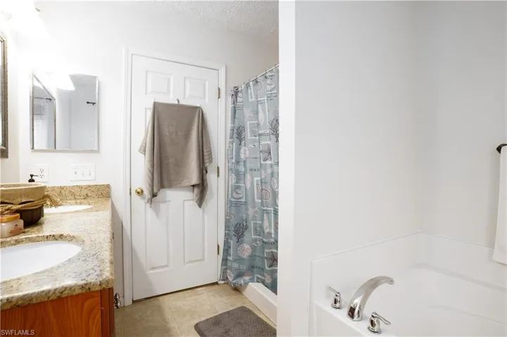 Bathroom with a tub, tile patterned floors, a textured ceiling, and double sink vanity