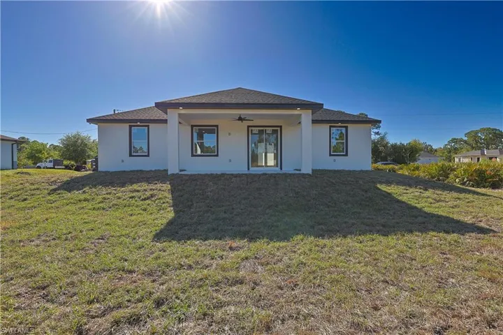 Back of property featuring stucco siding, a lawn, and ceiling fan